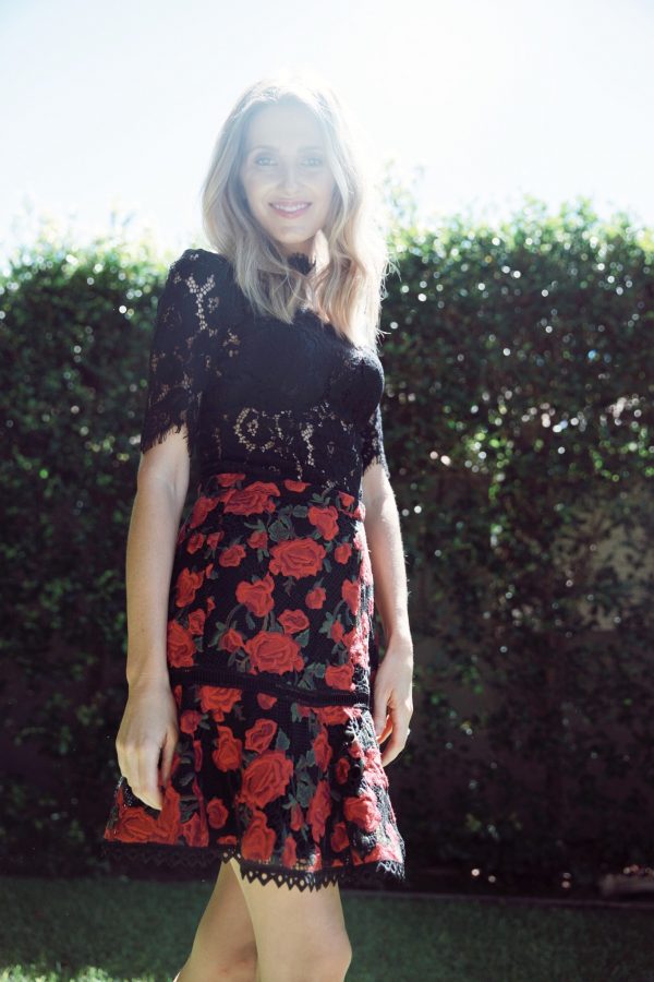 Kate Waterhouse walking in a garden wearing a Rodeo Show Uma lace tee and Rodeo Show Rosette skirt with red roses